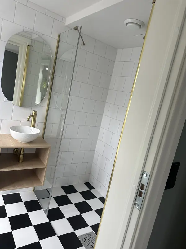 Bad med hvite veggfliser, sjakkrutete gulv i svart og hvitt og detaljer i messing